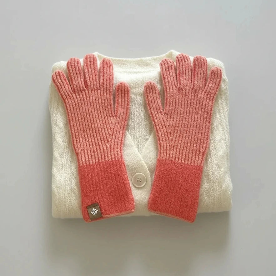 Pair of coral pink gloves on a folded cream sweater with a gray background